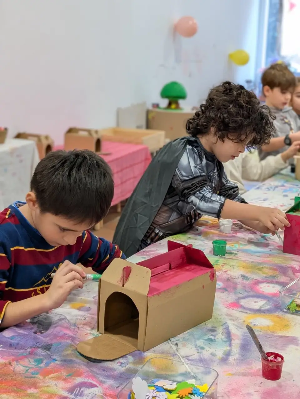 Children painting cardboard houses at the table in an after-school art class