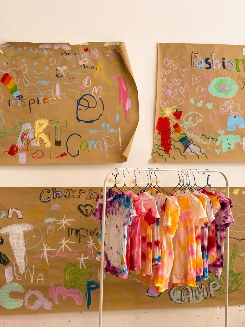 Tie-dyed T-shirts made at art camp, hanging in front of the campers' own painted paper murals