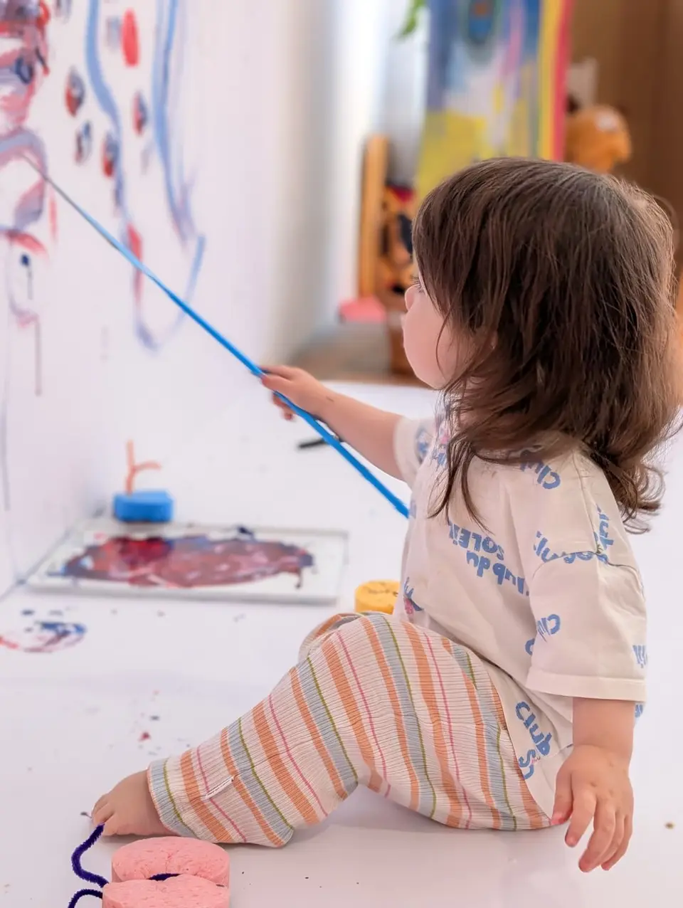 A toddler painting with a brush on a large sheet of paper at PlayMakers art playgroup